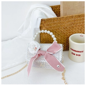 Detail of sequin mini bag featuring pearl handle, pink ribbon bow, and white flower charm