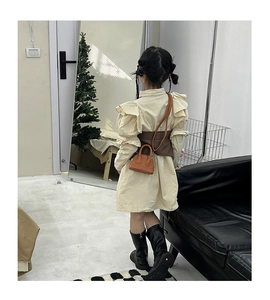 Detail of a girls beige ruffle dress paired with a dark brown belt and matching mini bag