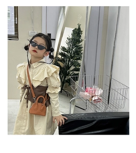 Detail view of a mini brown leather shell crossbody bag paired with a beige ruffle dress