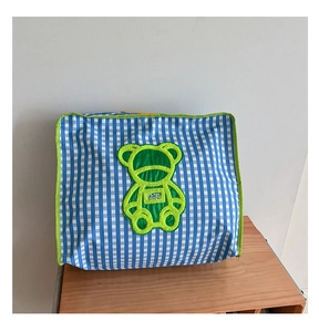 Close-up of blue plaid quilt storage bag with a green bear patch on a wooden cabinet