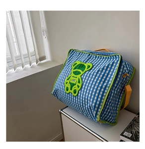 Close-up of blue plaid quilt bag featuring a green bear patch and yellow straps