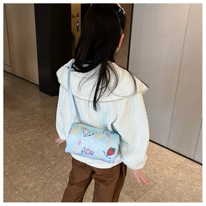 Close-up of a blue cartoon cylinder crossbody bag with rabbit prints worn by a child