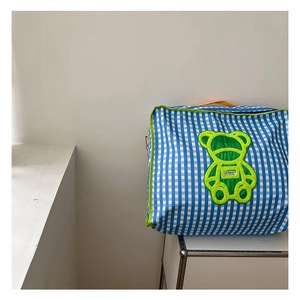 Detail of blue plaid children's storage bag with neon green bear patch and orange handle