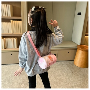 Pink cylinder canvas crossbody bag with cartoon bear print on a child model's shoulder