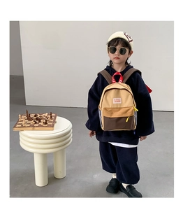 Detail view of khaki and brown color-block backpack with red straps worn by a young boy