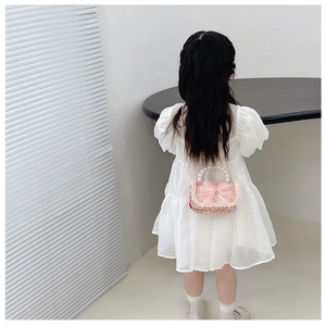 Pink girls crossbody bag with large mesh bow, pearl handle, and gold chain strap close-up