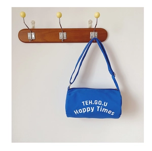 Détail du sac cylindrique en toile bleue avec lettres blanches et bandoulière réglable