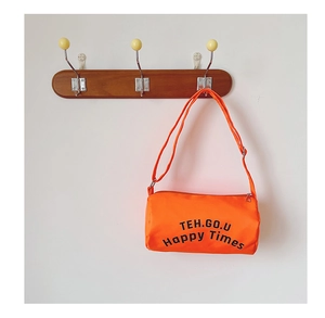 Détail du sac cylindrique orange vif avec lettrage noir et bandoulière réglable