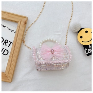 Detail of pink sequin girl's bag with mesh bow, heart gem and pearl handle on white fabric