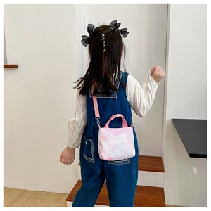 Fillette portant un sac à bandoulière rose avec ours en toile, vue de dos en intérieur