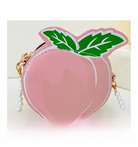 Detail of pink peach-shaped crossbody bag with green leaf decor and pearl chain strap