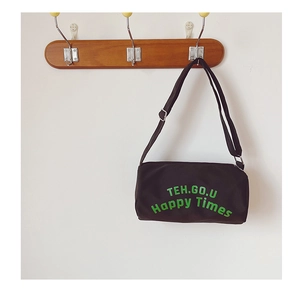 Détail du sac cylindrique en toile noire avec imprimé de lettres vertes et sangle réglable