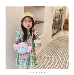 Pink round crossbody bag with iridescent shell and wings worn by a child model