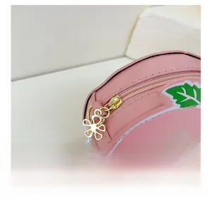Detail of pink patent leather peach bag featuring a gold flower zipper and pearl strap