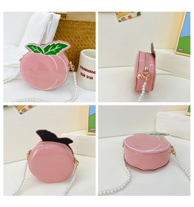 Detail view of pink peach shaped crossbody bag with pearl chain and green leaf accents