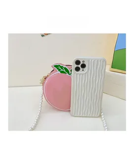 Detail of peach-shaped girls handbag with pearl chain next to phone for size comparison