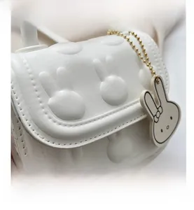 Detailansicht der weißen Mini-Handtasche mit Hasenprägung und süßem Anhänger-Detail