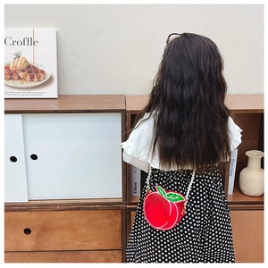 Detail of red apple girl handbag with green leaf accent and white pearl strap