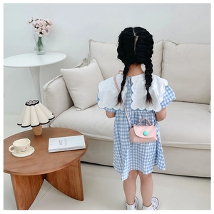 Detail of pink mini crossbody bag with green button on girl blue checkered dress