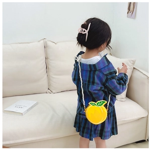 Detail of yellow fruit-shaped kids bag with green leaf and white pearl chain strap