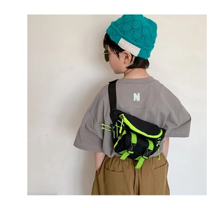 Detail of kids black canvas chest bag with neon green accents shown on a young model