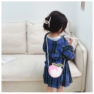 Girl wearing a peach-shaped crossbody bag with pearl strap and matching pink hair clip