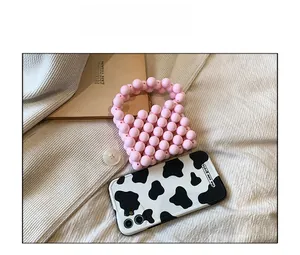 Pink beaded mini handbag next to a black and white cow print phone case on fabric