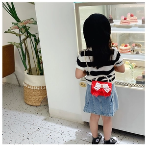 Fillette portant un sac à main rouge avec nœud en dentelle devant une vitrine de pâtisserie