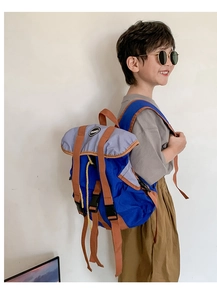Close-up of a stylish boy wearing a blue and purple color-block canvas backpack outdoors