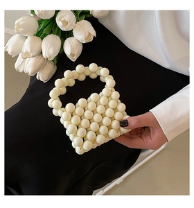 Detail view of handmade white pearl beaded mini handbag held against black dress background