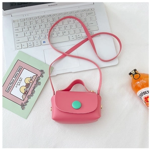 Flat lay of a mini pink PU leather crossbody bag with a green button on a white desk
