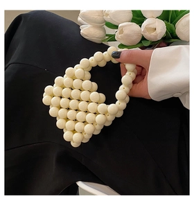 Detailed view of elegant ivory faux pearl mini handbag held by hand with tulips