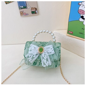 Détail d'un sac fille en dentelle vert clair avec poignée en perles et nœud avec pierre verte