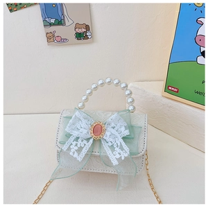 Détail du mini sac en dentelle blanche avec nœud vert, poignée en perles et chaîne d'or
