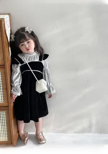 Detail view of girls black velvet vest dress with grey ruffled long sleeve top and pearl bag