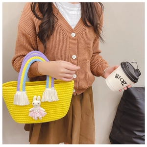Detail of yellow woven bucket bag featuring rainbow handles and white tassel accents