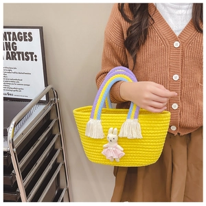 Detail of yellow woven kid handbag featuring rainbow handle and cute bunny pendant charm