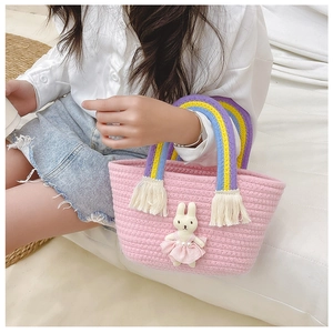 Detail of pink woven straw tote bag with rainbow handles and a cute bunny doll charm