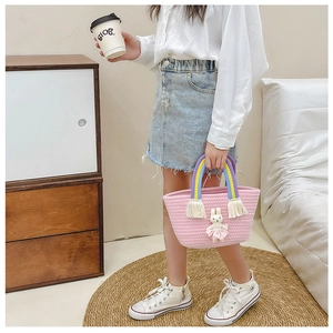Pink woven straw bag with rainbow handle and cute bunny doll held by a young child