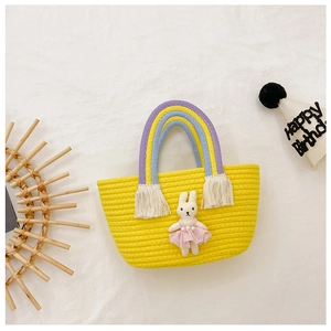 Detailed view of yellow woven straw bag with rainbow handle and plush bunny charm