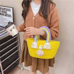 Handmade yellow straw basket bag for kids featuring a cute bunny doll and rainbow tassels