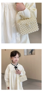 Detailed close-up of white faux pearl woven handbag with elegant top handle and large bead