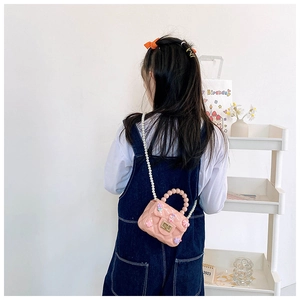Vista posteriore di una bimba con borsa in silicone rosa, tracolla di perle e ciondoli cartoon