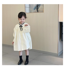 Girl's white long-sleeve dress detail with black bow and woven pearl handbag accessory