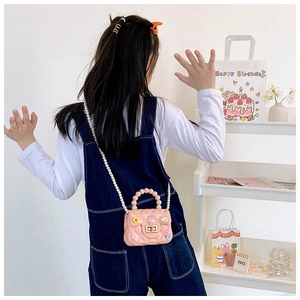 Pink jelly crossbody bag with pearl handle and cute cartoon charms on girl's back