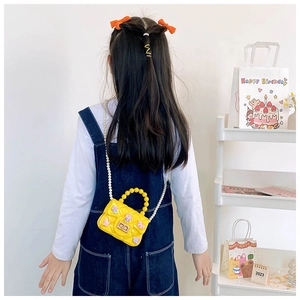 Dettaglio borsa bimba in silicone giallo con manico in perle e patch cartoni