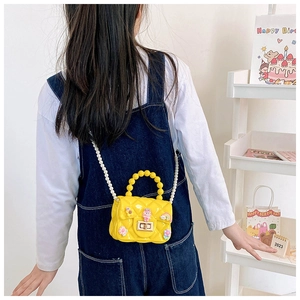 Detail of yellow jelly crossbody bag with cute cartoon charms and white pearl strap