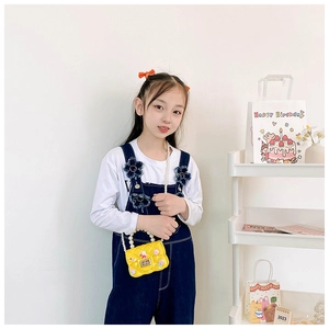 Detail of yellow toddler crossbody bag with pearl handle and cartoon charms on model