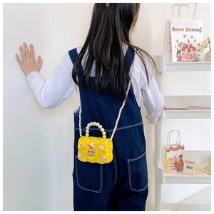 Detail of yellow quilted rabbit cross-body bag with pearl handle worn by a girl