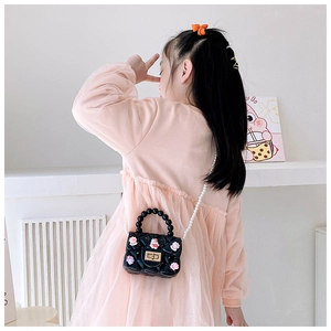 Vista posteriore di una bimba con borsa jelly nera, fiori e catena di perle